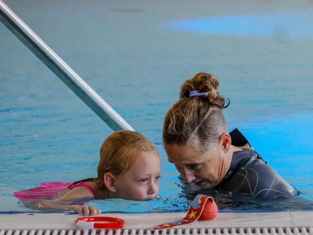 Zweminstructeur geeft een kind rustig en persoonlijk aandacht aan de badrand