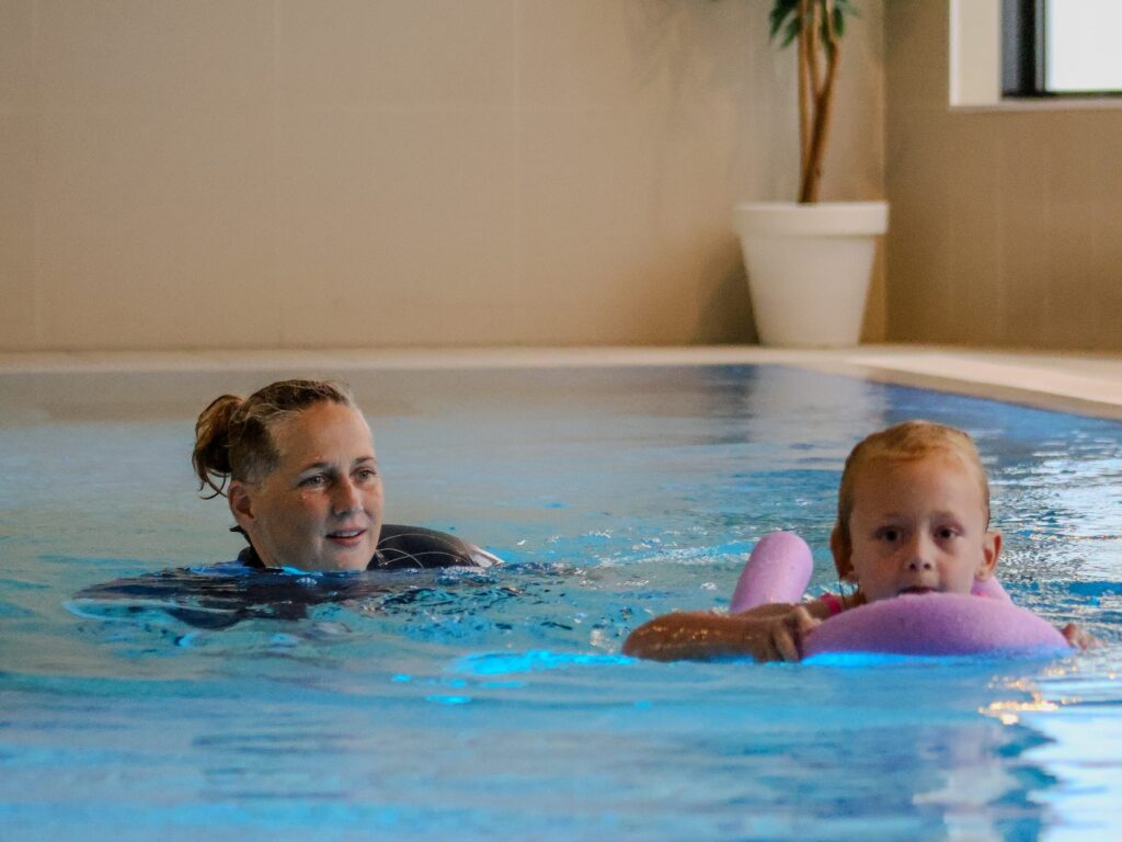 Zweminstructeur staat naast een kind in het water tijdens zwemles